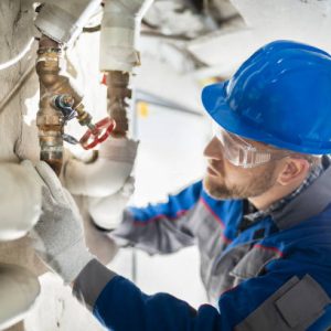 Male Worker Inspecting Water Valve For Leaks In Basement